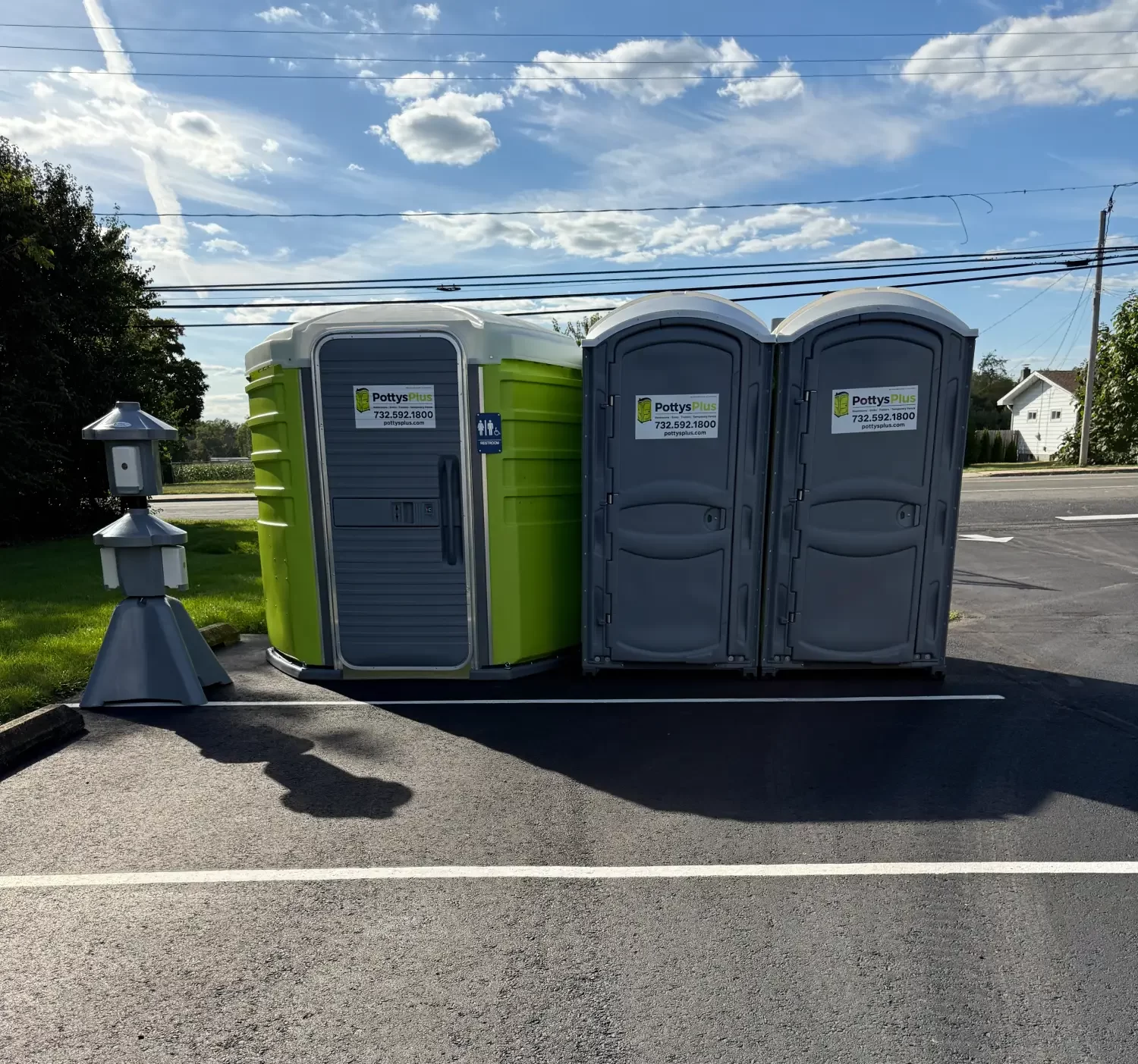 Green ADA compliant and two grey portable toilets parked in a lot.