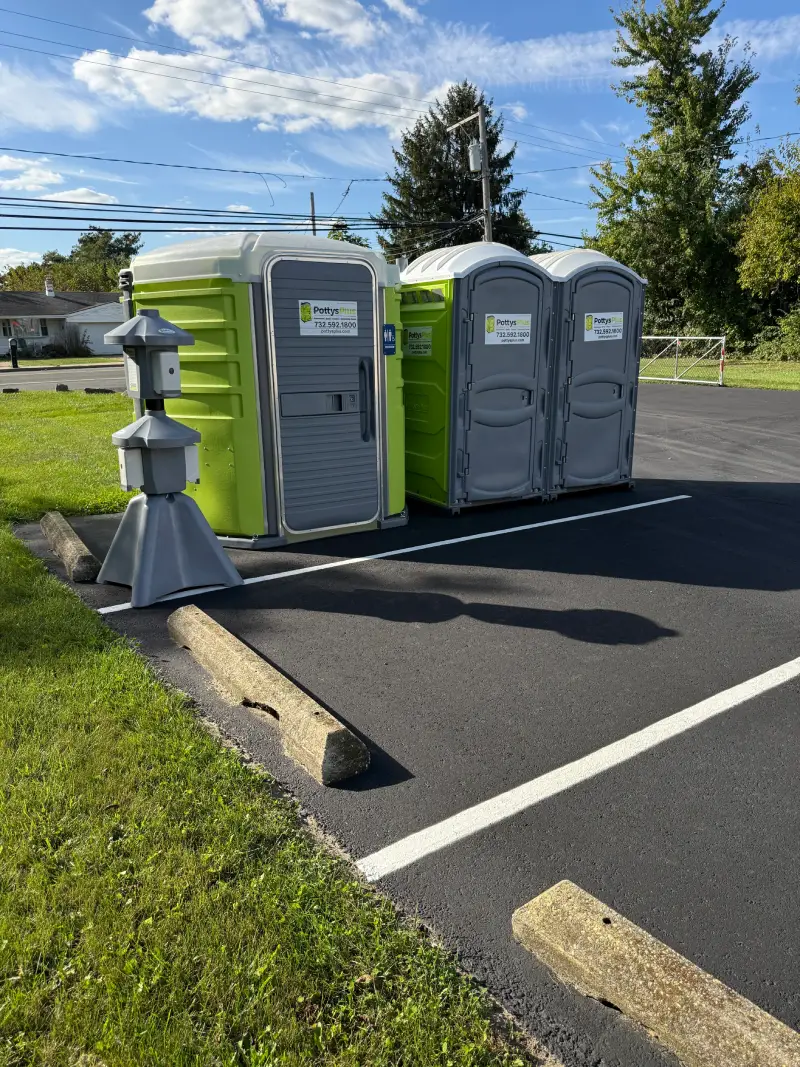 Green ADA unit and grey portable toilets with a hand sanitizer station.
